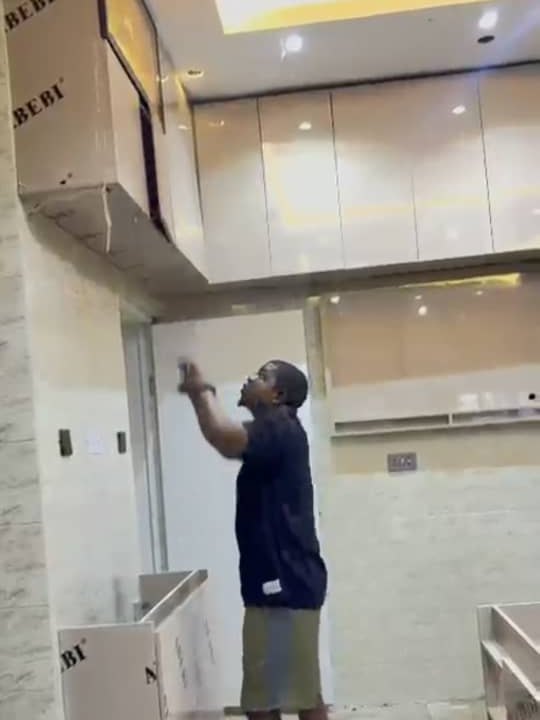 A fitter reaching up to align a wall unit against the ceiling of a kitchen under installation
