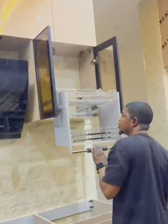 A pull-down dish rack being fitted inside a wall cabinet with a bronze glass door